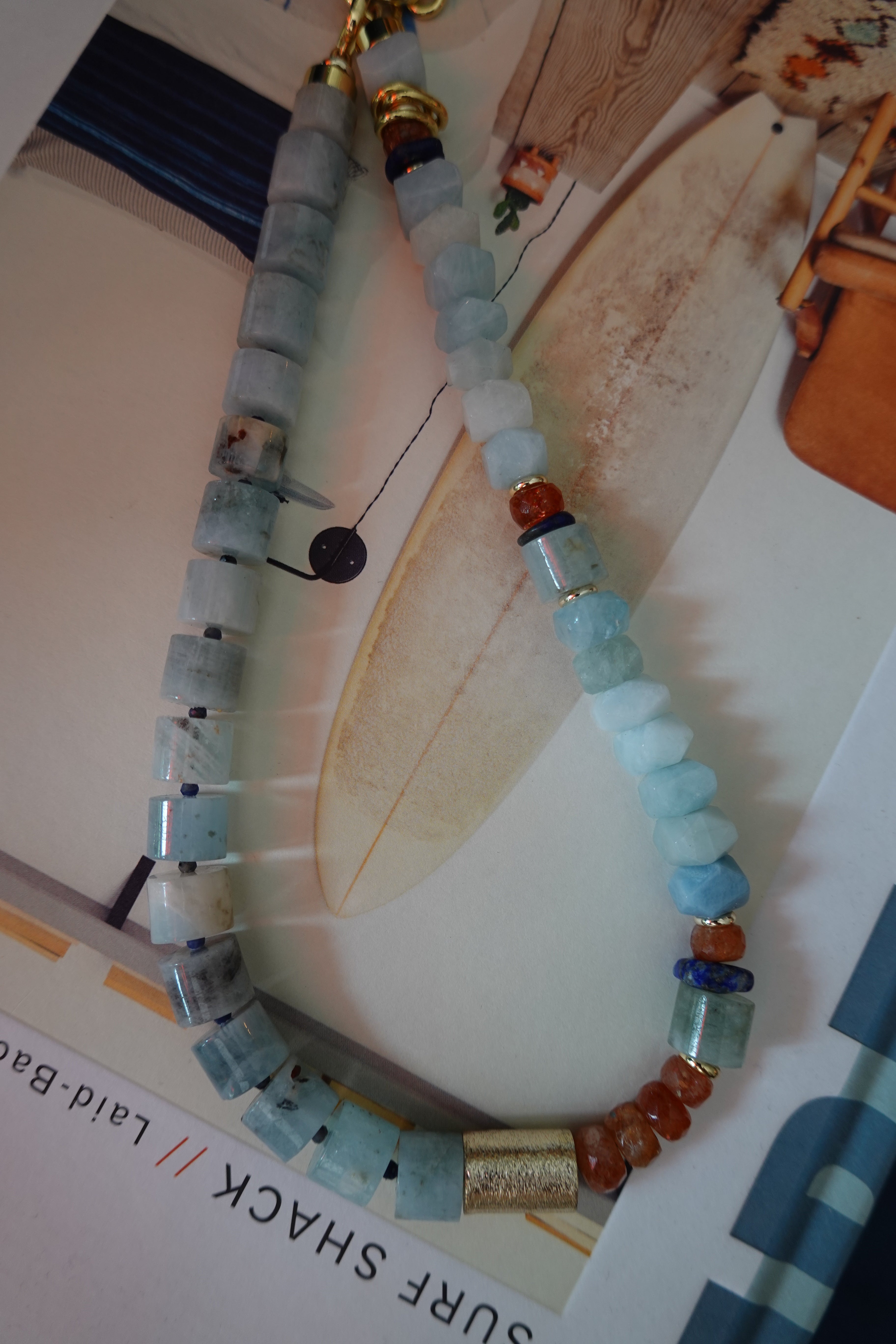 Beaded necklace on a surfboard with a magazine underneath